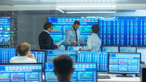 Business people surrounded by computer screens featuring graphs related to trade confirmations